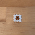 A small cross-stitch sample featuring a brown bear on white fabric, placed on a light wood surface.